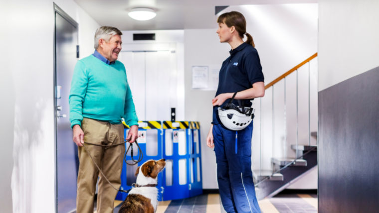Elevator technician in a hallway conversing with a man with dog - KONE Modernization